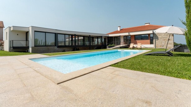 Een modern huis met een zwembad, een overdekt terras en een stenen muur.