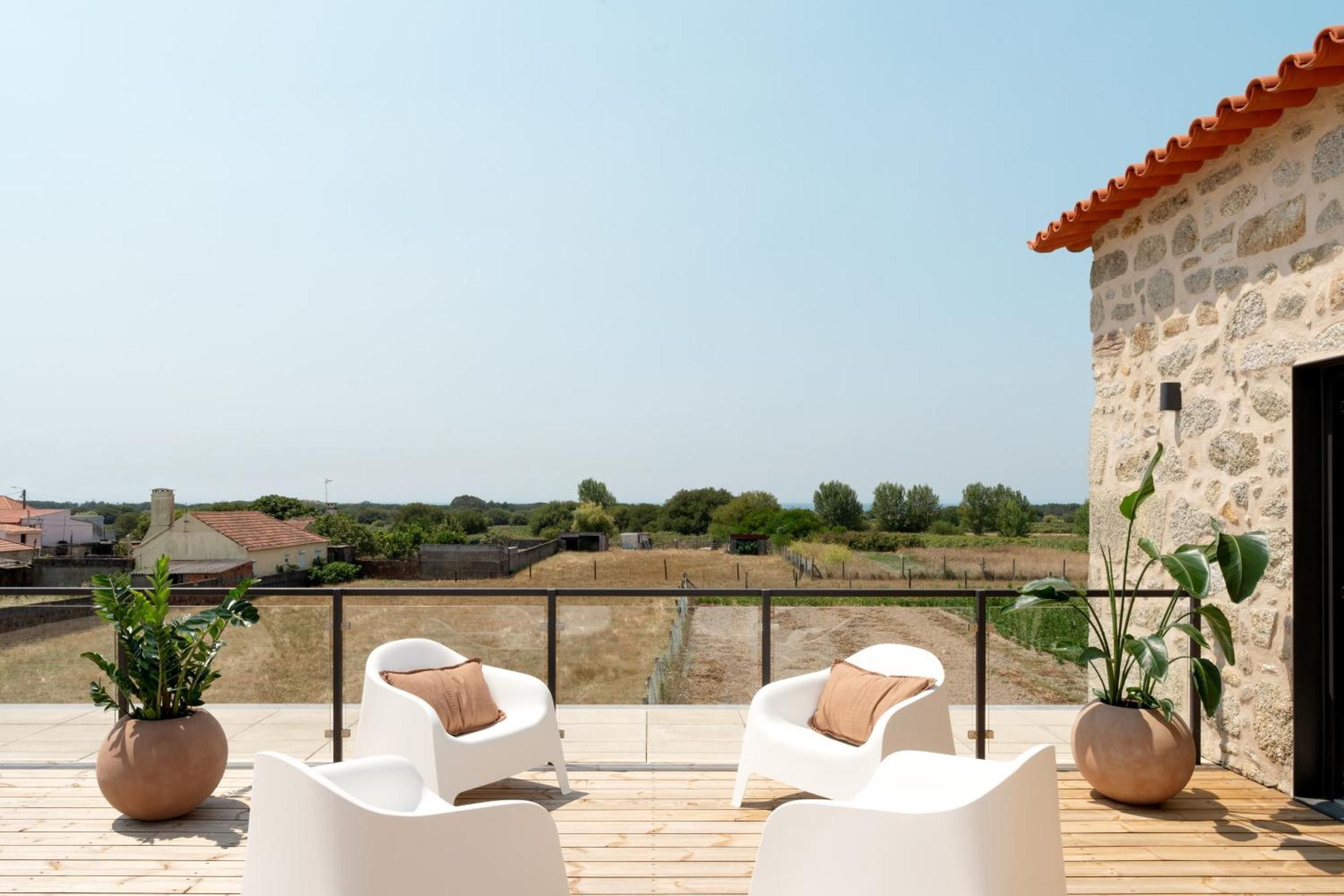 A terrace with white chairs and potted plants, overlooking a rural landscape.