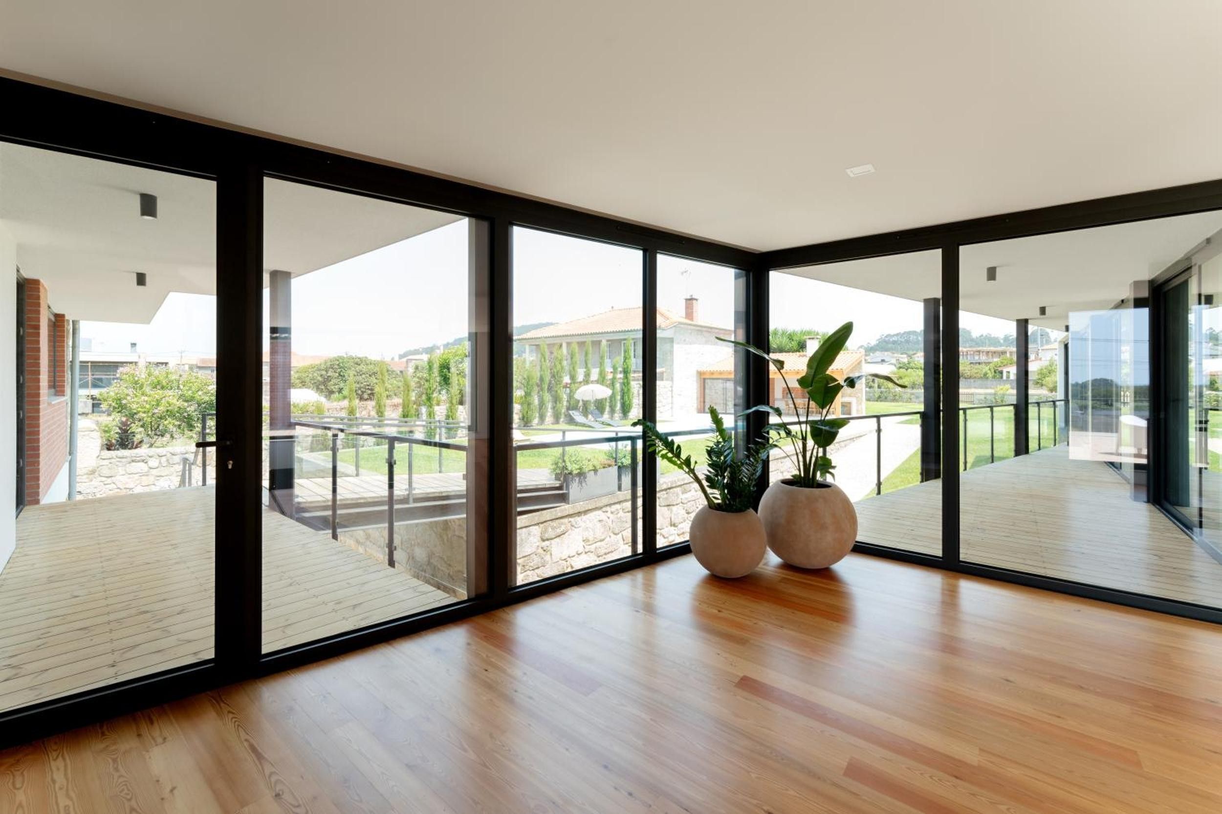 Een ruime kamer met grote glasramen, houten vloeren en twee potplanten.