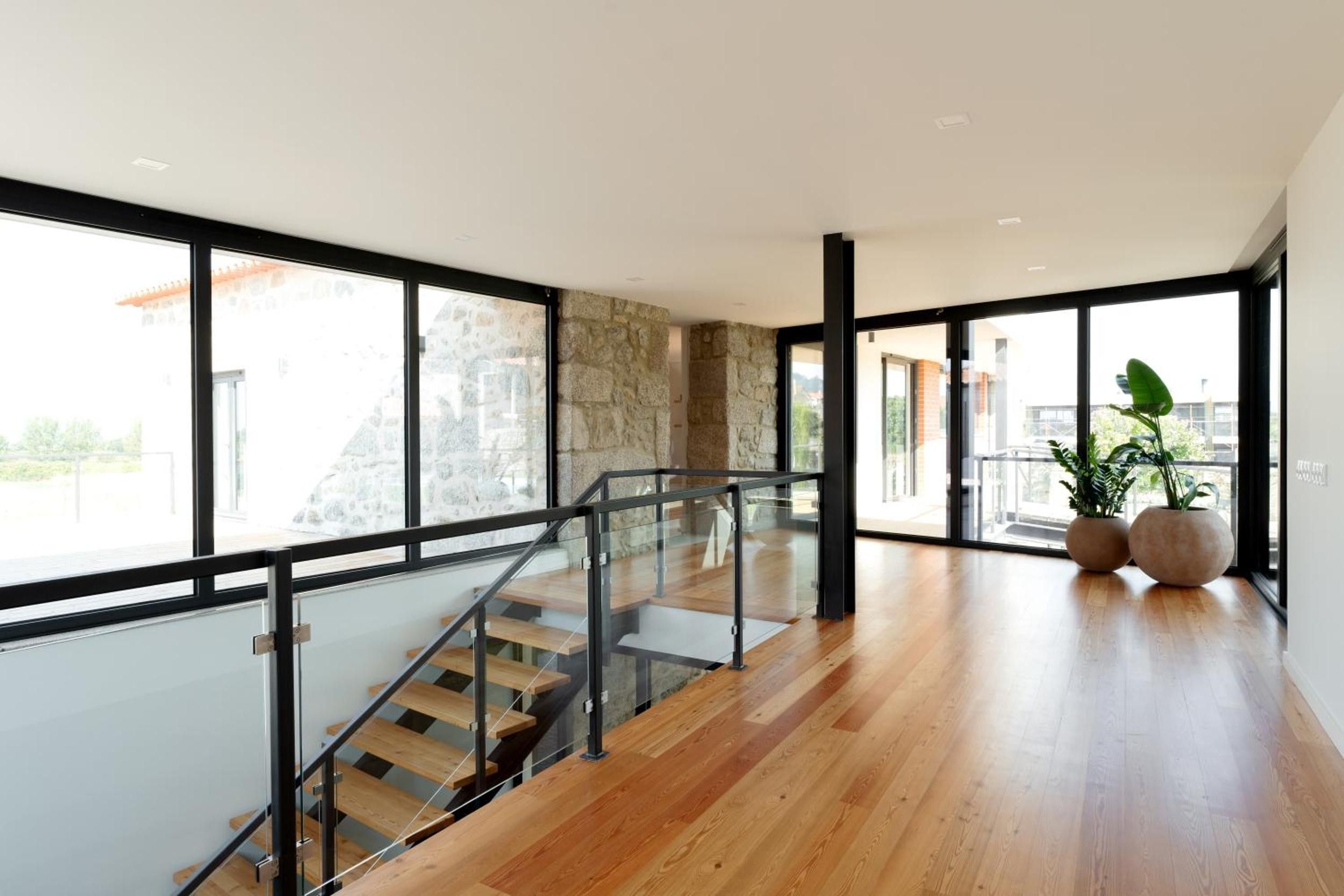 Un interior moderno con una escalera de madera, ventanas amplias y una pared de piedra.