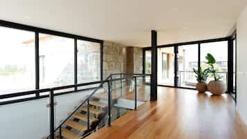 Un interior moderno con una escalera de madera, ventanas amplias y una pared de piedra.