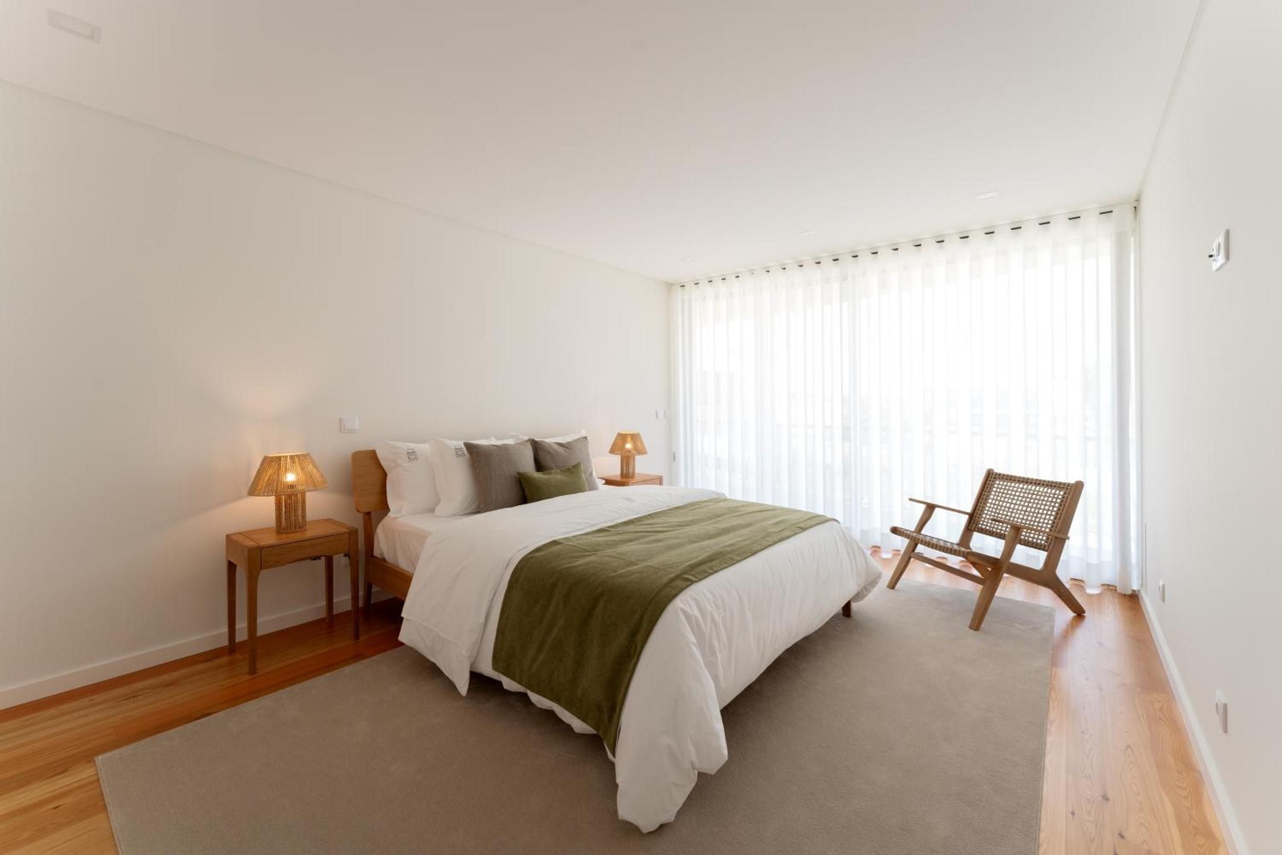 A bedroom with a bed, two bedside tables, a chair, and a window with curtains.
