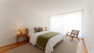 A bedroom with a bed, two bedside tables, a chair, and a window with curtains.