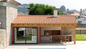 Een modern huis met een zwembad, een overdekt terras met een tafel en stoelen, en een stenen muur.