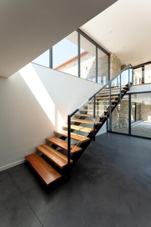 Una escalera moderna con peldaños de madera y barandillas de metal, que conduce a un nivel superior con ventanales amplios.