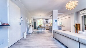 Una cocina moderna con una isla central, un comedor con sillas traslúcidas y una sala de estar con sofá.