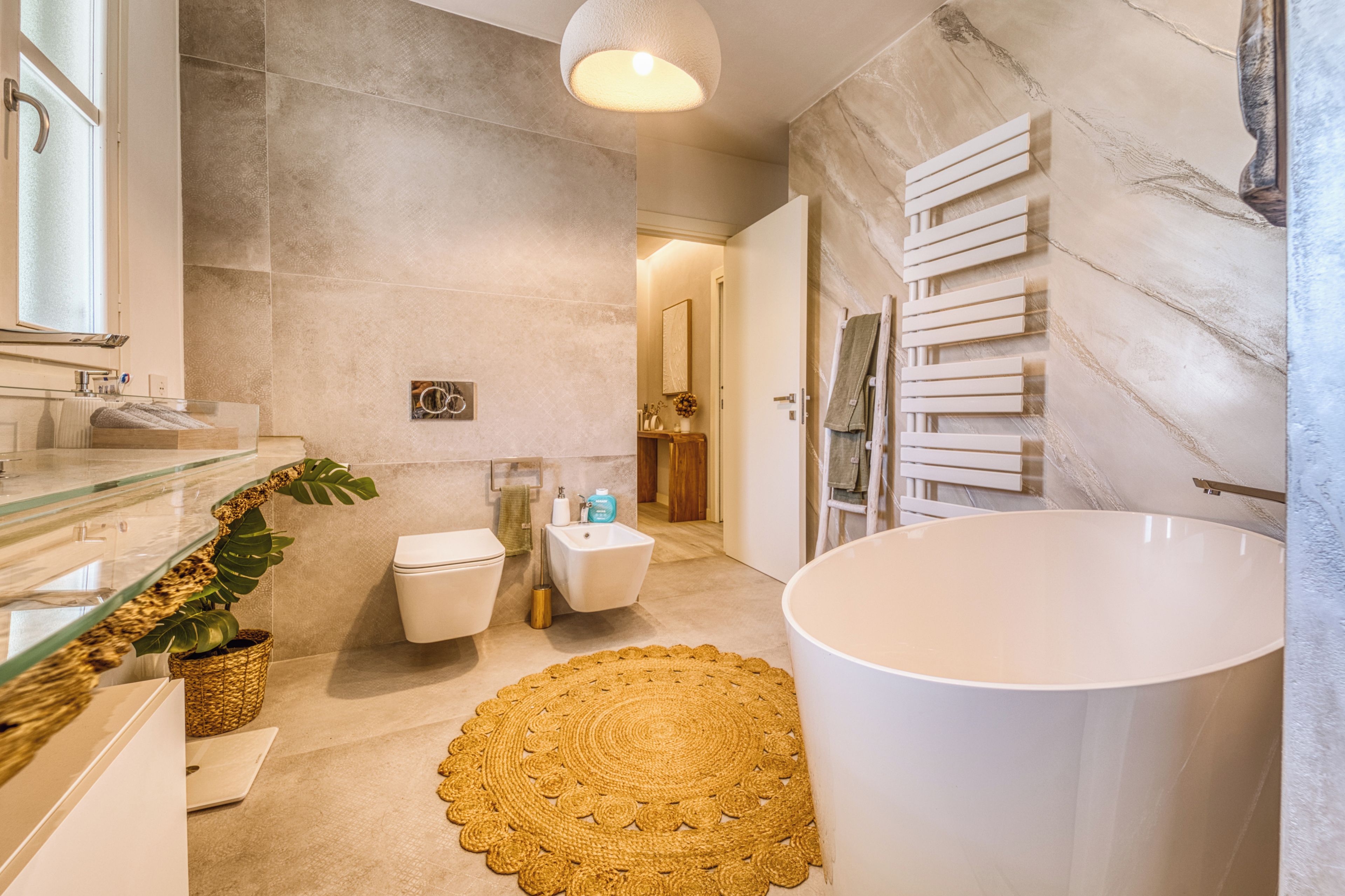 Un baño moderno con cabina de ducha de vidrio, inodoro independiente, bidé, lavamanos grande de color blanco y una alfombra decorativa dorada.