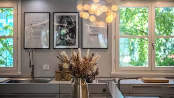A kitchen with a vase of dried plants on the counter, a sink, and framed pictures on the wall.