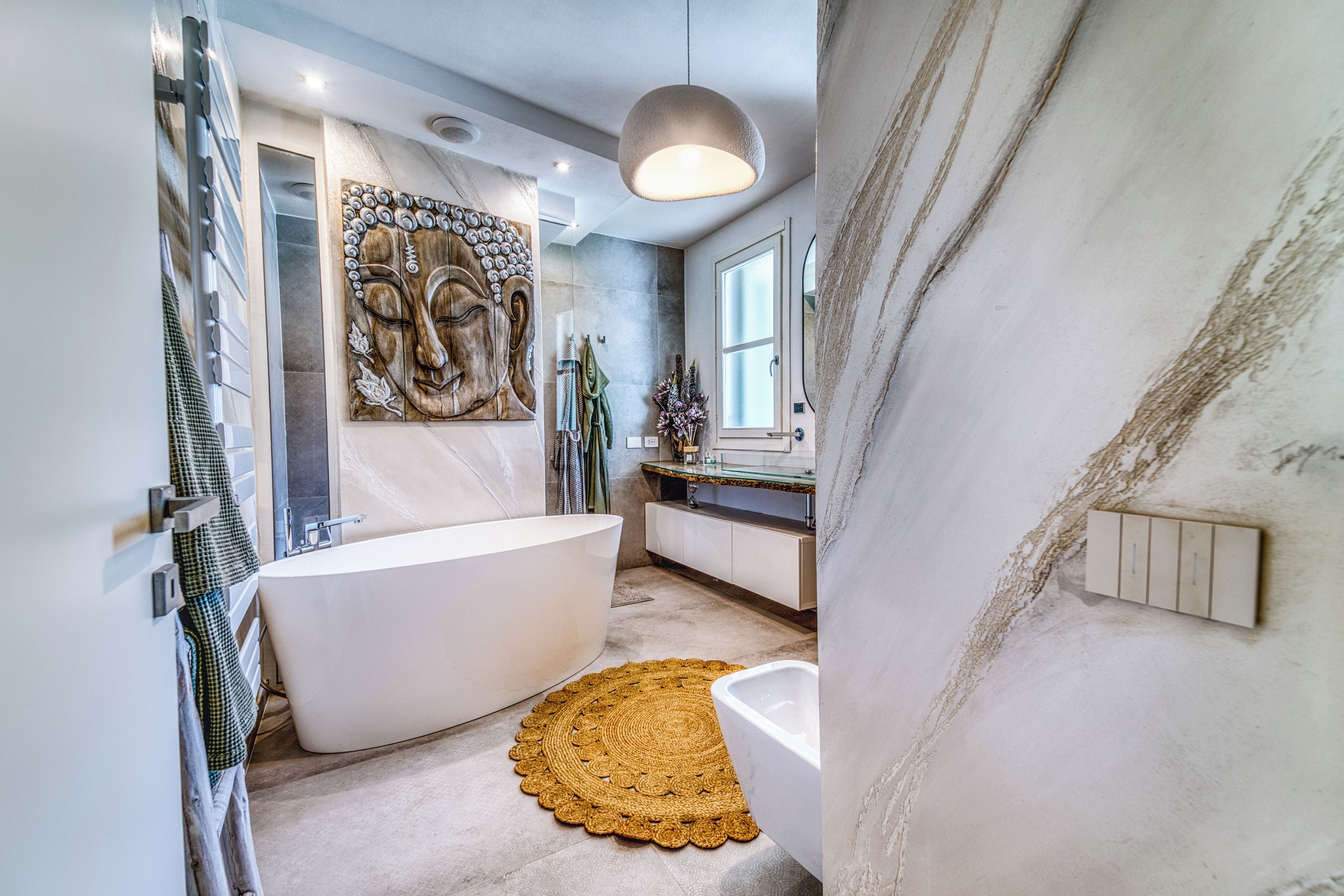 A modern bathroom with a freestanding bathtub, a glass shower enclosure, and a decorative wall piece.