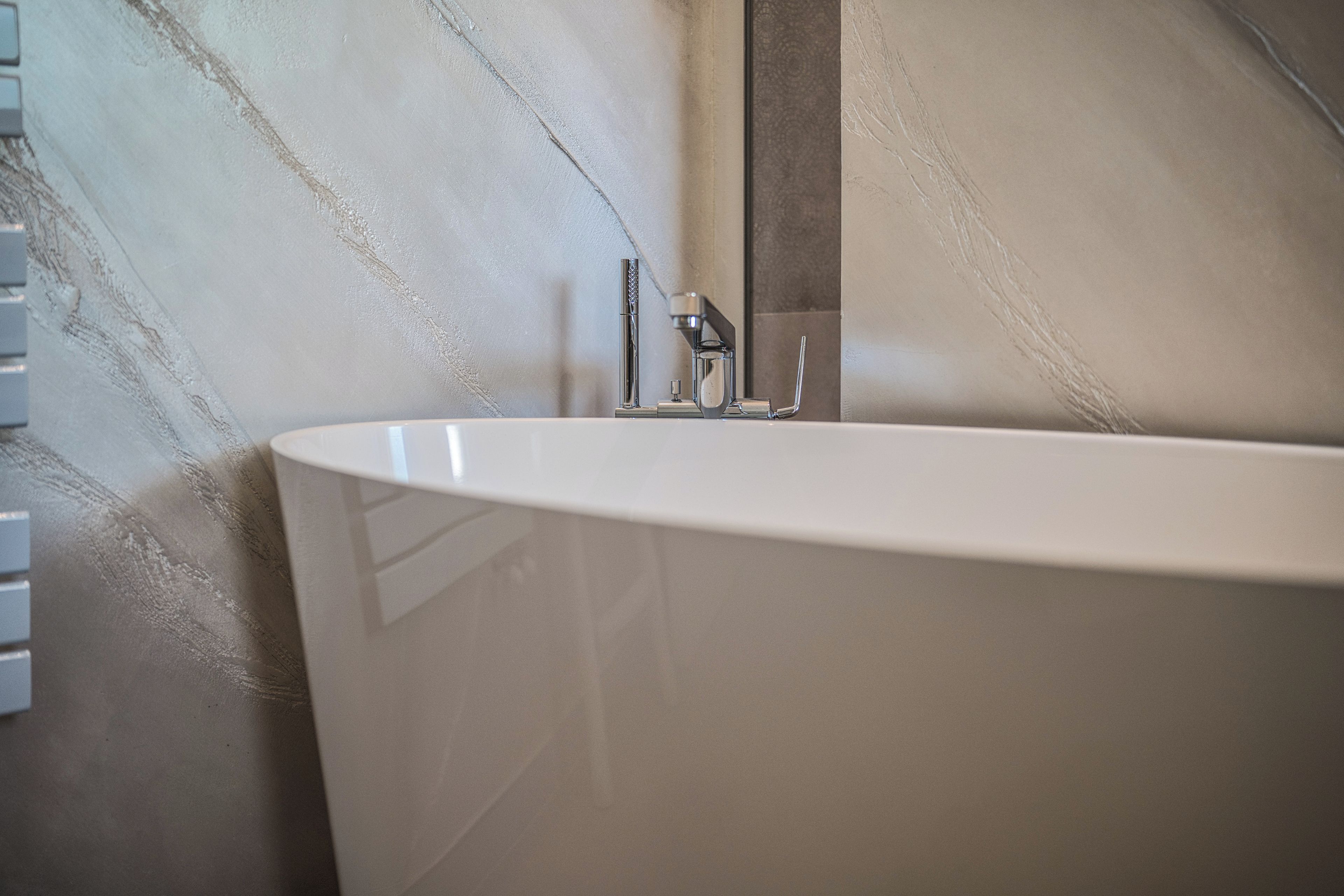 Un baño moderno con una bañera independiente, un grifo de pared y una pared con textura.