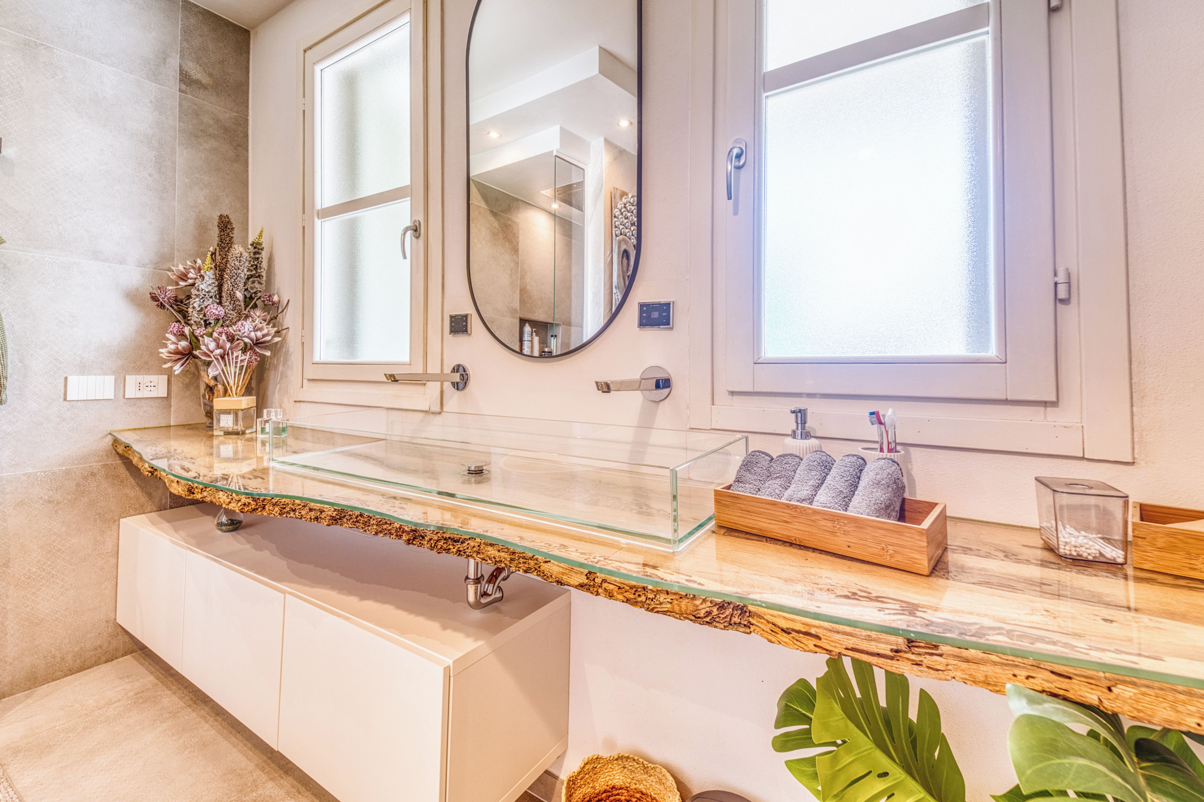 Une salle de bain avec un plan de toilette en verre, deux vasques, un miroir et une boîte en bois contenant des articles de toilette.
