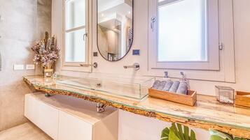 Une salle de bain avec un plan de toilette en verre, deux vasques, un miroir et une boîte en bois contenant des articles de toilette.