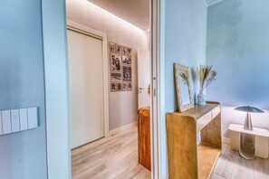 Un pasillo con suelo de madera, una puerta blanca y un muro con cuadros enmarcados.