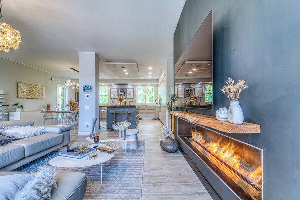 A modern living room with a fireplace, a dining area, and a kitchen in the background.