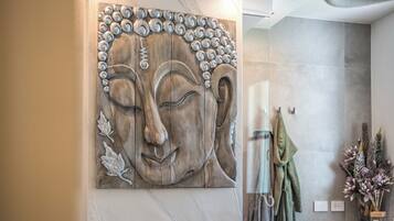 Una parete con un'ampia scultura in legno raffigurante un volto, un portascopevoli con asciugamani e un vaso con fiori.