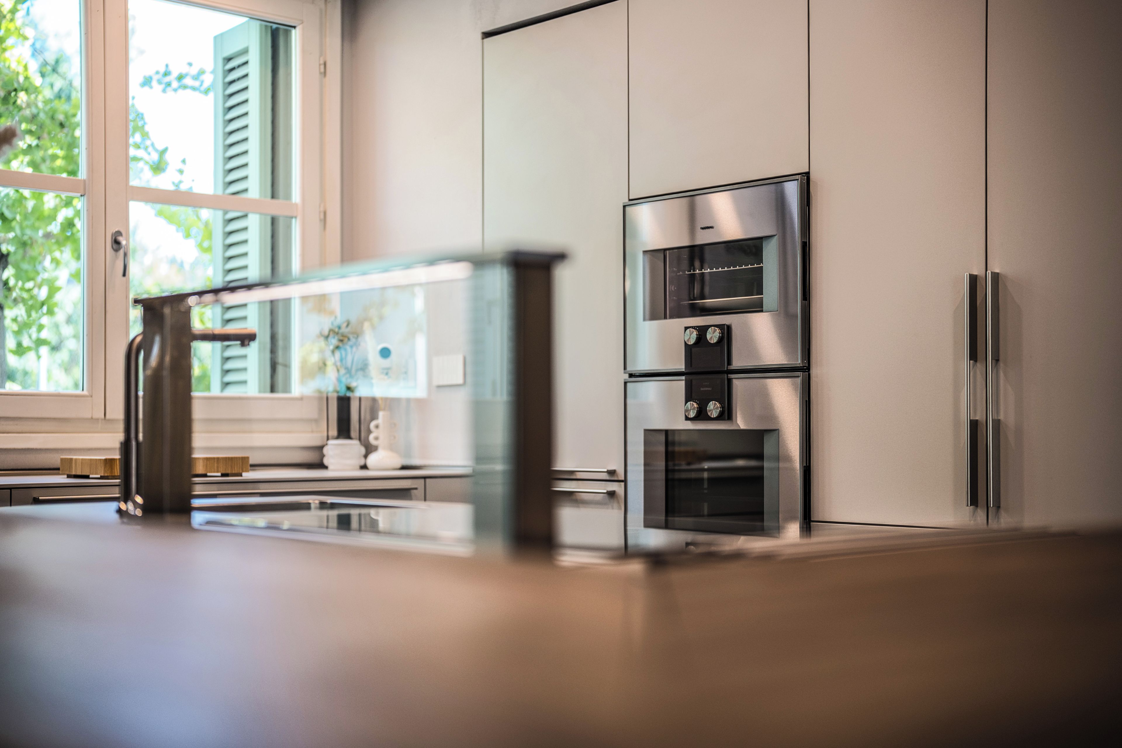 A modern kitchen with stainless steel appliances, including a refrigerator, oven, and microwave, and a window with shutters.