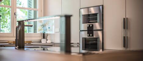 A modern kitchen with stainless steel appliances, including a refrigerator, oven, and microwave, and a window with shutters.