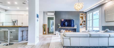 A modern living room with a large TV, a fireplace, and a kitchen area with bar stools.