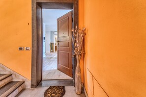 A hallway with a wooden door leading to a room, a staircase, and a decorative vase with dried plants.