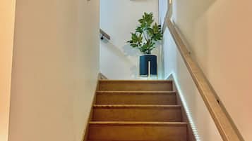 Uma escada de madeira com corrimão, um quadro na parede e um vaso de planta no topo.