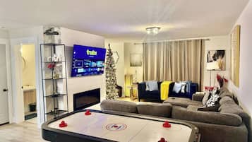 A living room with a flat-screen TV, a foosball table, a sofa, and a Christmas tree.