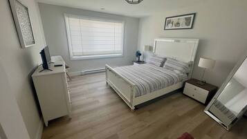 A bedroom with a bed, bedside tables, a desk, a chair, a window with blinds, and a ceiling light fixture.