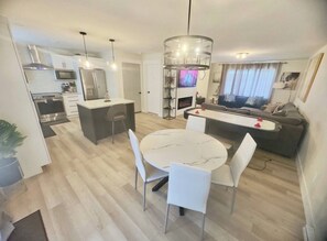 A modern living space with a kitchen, dining area, and a seating area with a TV. - Stylish 3BR Home Near Moncton Airport Free Parking (Dieppe)