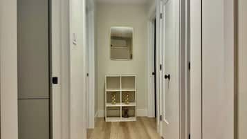 Um corredor com portas brancas, um espelho na parede e uma prateleira com objetos decorativos.