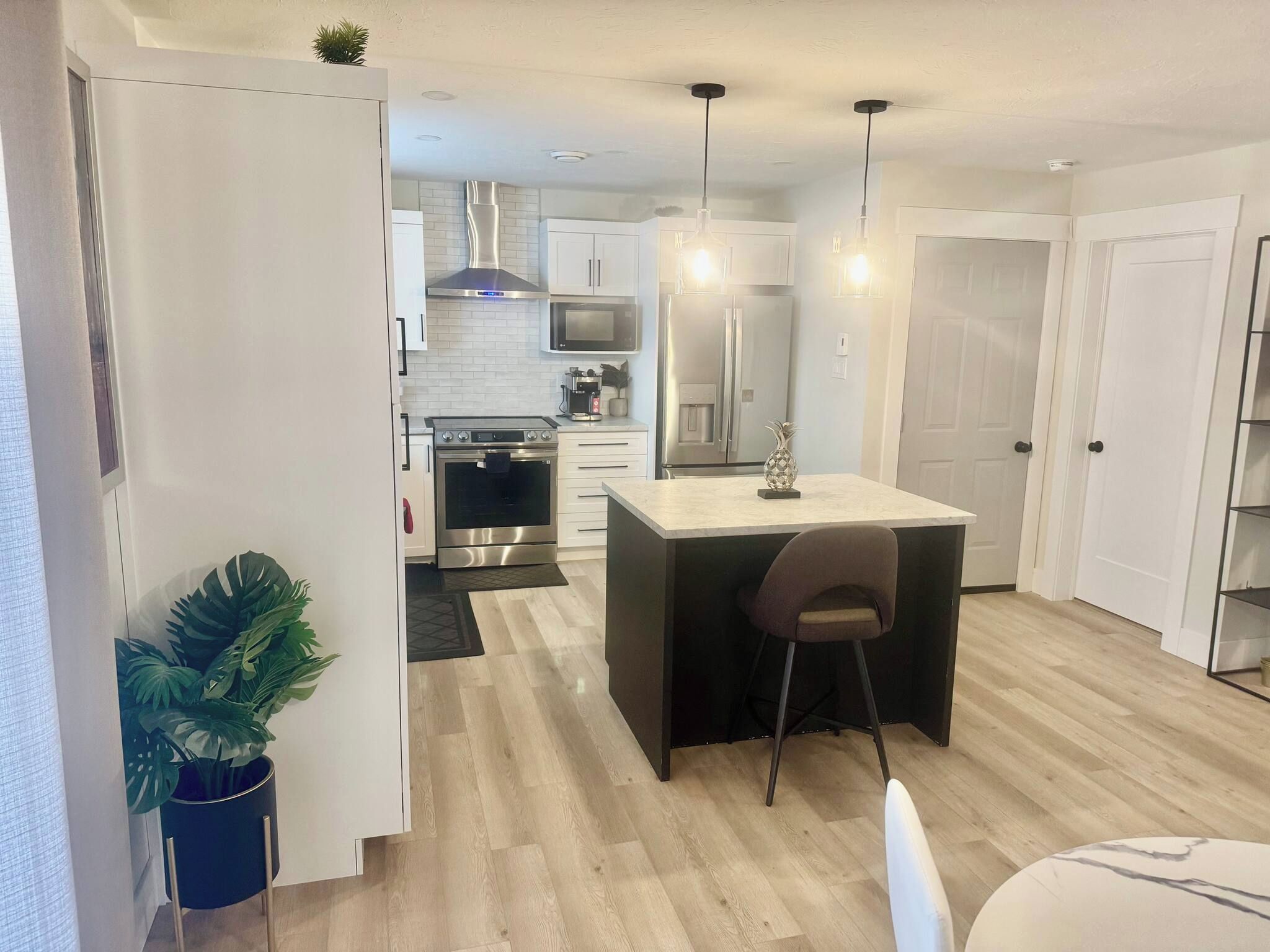 Une cuisine moderne dotée d’un îlot central, d’appareils électroménagers en acier inoxydable et de luminaires suspendus.