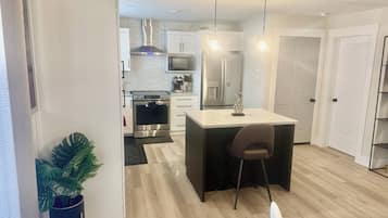 Une cuisine moderne dotée d’un îlot central, d’appareils électroménagers en acier inoxydable et de luminaires suspendus.