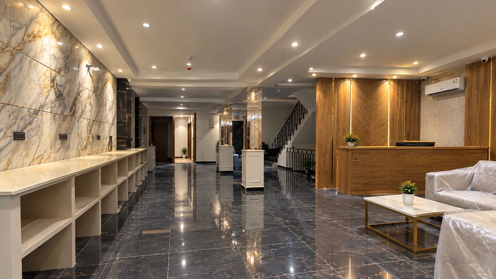 A hotel lobby with a marble reception desk, a reception area with a wooden panel wall, a staircase, and a seating area with a white sofa.