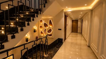 A hotel corridor with a marble floor, a staircase with black railings, and recessed lighting.