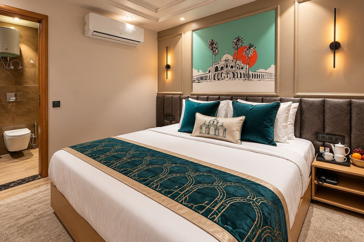Habitación de hotel con una cama grande, cabecera con una pintura de un paisaje urbano, mesita de noche con frutero y baño con ducha e inodoro.