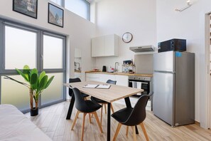 A modern kitchen with a dining area, a refrigerator, and a potted plant.