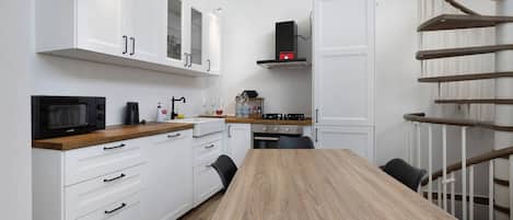 A modern kitchen with white cabinetry, a wooden dining table, and a built-in stove.