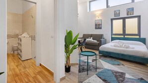 Une chambre d’hôtel moderne, équipée d’un lit, d’un canapé, d’une petite table, d’une plante et offrant une vue sur la ville par la fenêtre.