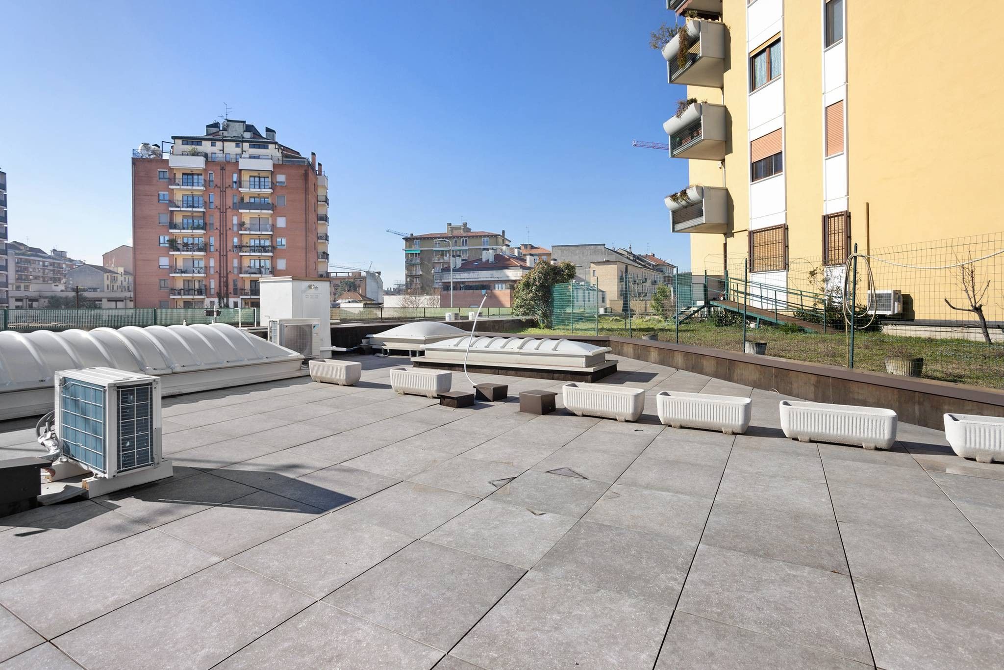 Una terraza en la azotea con unidades de aire acondicionado al aire libre, zonas de estar y vistas de los edificios circundantes.