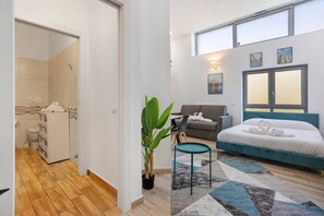 Una moderna camera d'albergo con un letto, una poltrona, un tavolino, una pianta e vista sulla città dalla finestra.