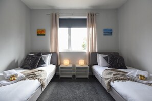 A twin room with two beds, a window with curtains, bedside tables with lamps, and wall art. - Spacious Portchester Home with Garden & Parking (Portchester)