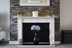 Ein Kamin mit Steinwand, weißem Sims und einer Vase mit Blumen.