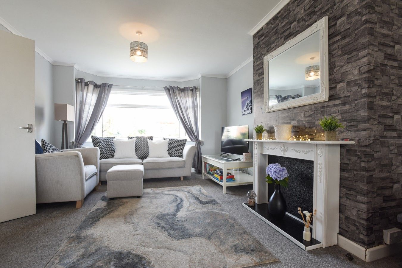 A modern living room with a fireplace, a sofa set, a television, and a stone accent wall.