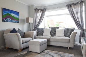 A living room with a sofa set, patterned cushions, a painting on the wall, and a view through the window. - Spacious Portchester Home with Garden & Parking (Portchester)