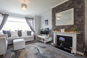 Ein modernes Wohnzimmer mit Kamin, einer Sofagarnitur, einem Couchtisch und einem Fernseher.
