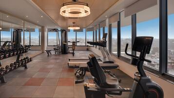Un gimnasio moderno con diverso equipo de ejercicio, amplias ventanas que ofrecen vistas a la ciudad y un diseño espacioso.