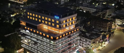 Un hotel de varios pisos con diseño moderno, que cuenta con una entrada destacada, varios balcones y vista al río.