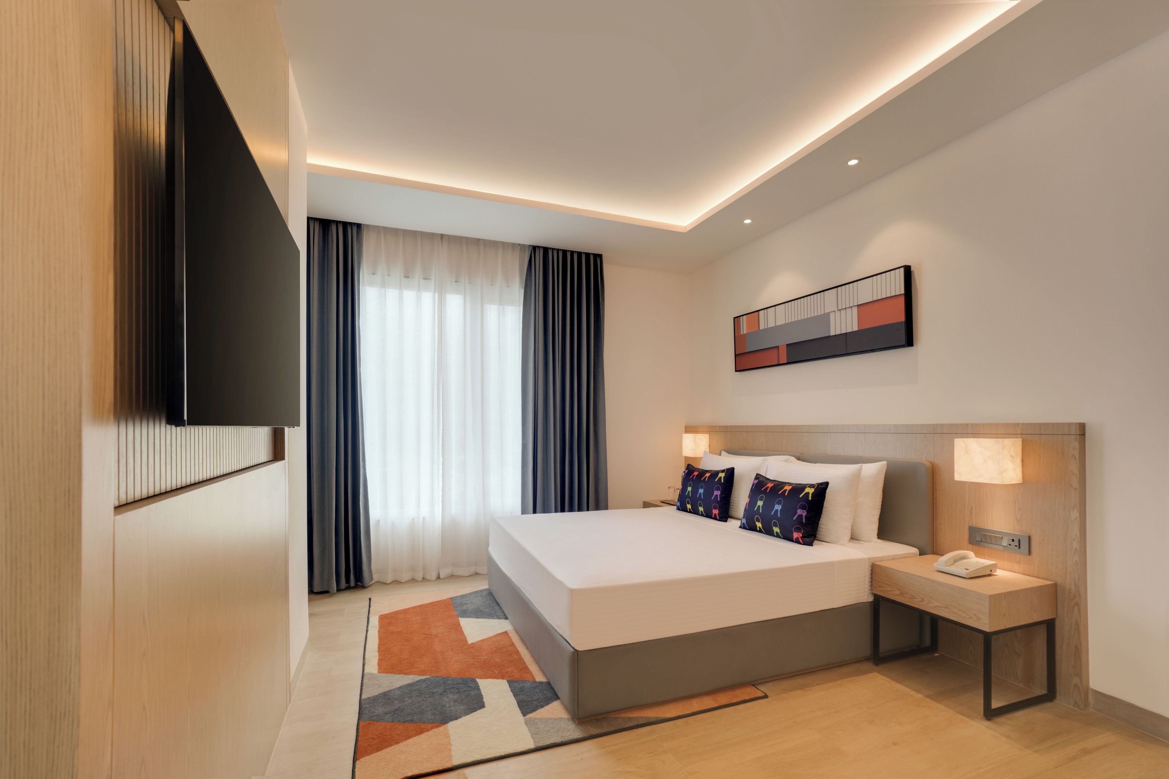 Ein modernes Hotelzimmer mit Bett, Nachttisch und einem wandmontierten Flachbildfernseher.