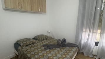 A bedroom with a bed, a wooden wardrobe, a window with curtains, and a light switch on the wall.