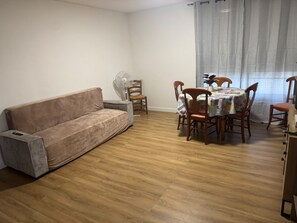 A living room with a sofa, a dining table with chairs, a fan, and a window with curtains. - Peaceful 4-bedroom apartment in welcoming Toulouse neighborhood (Toulouse)