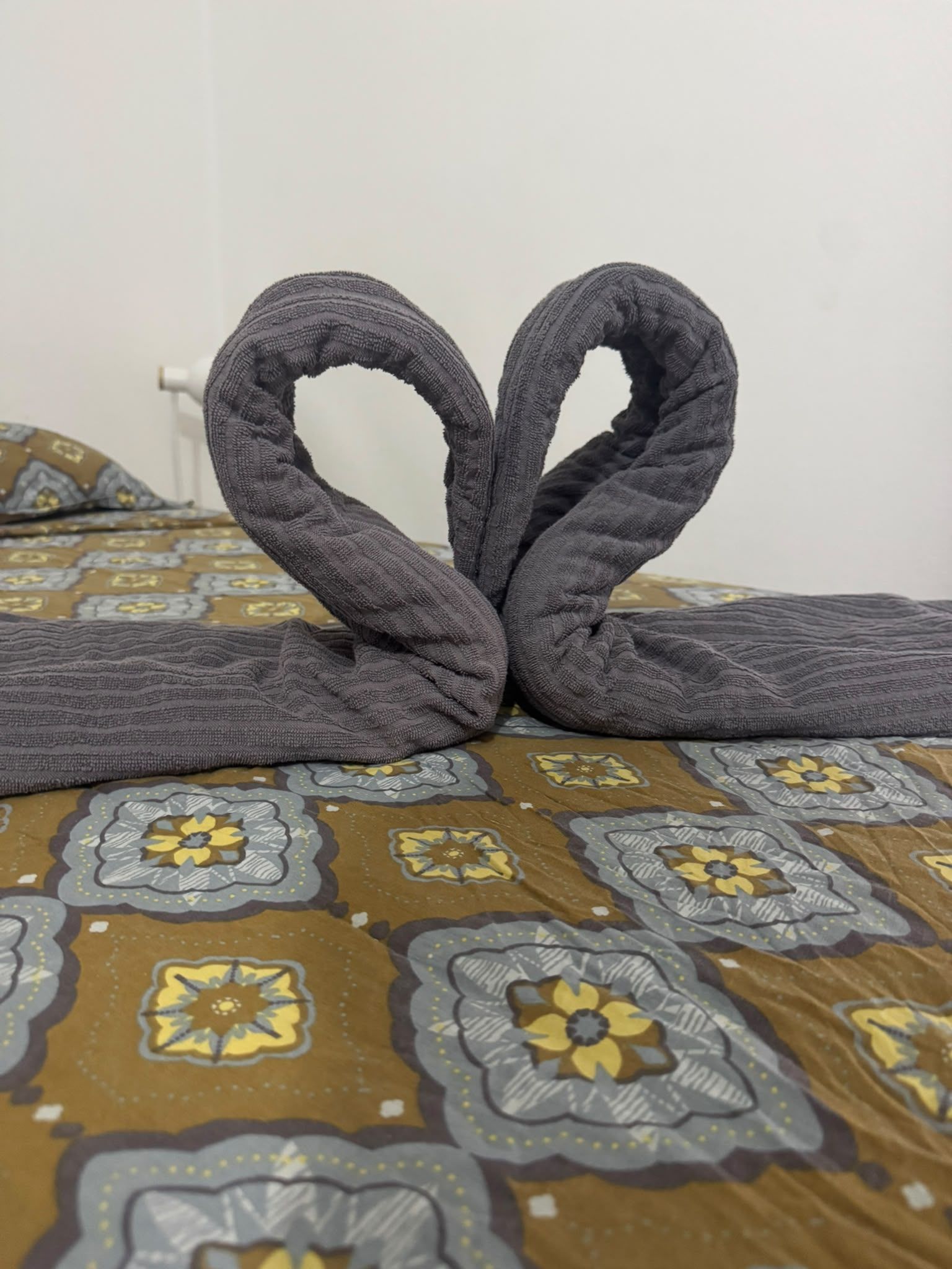 Un lit avec une couvre-lit à motifs et une serviette disposée en forme de cœur.