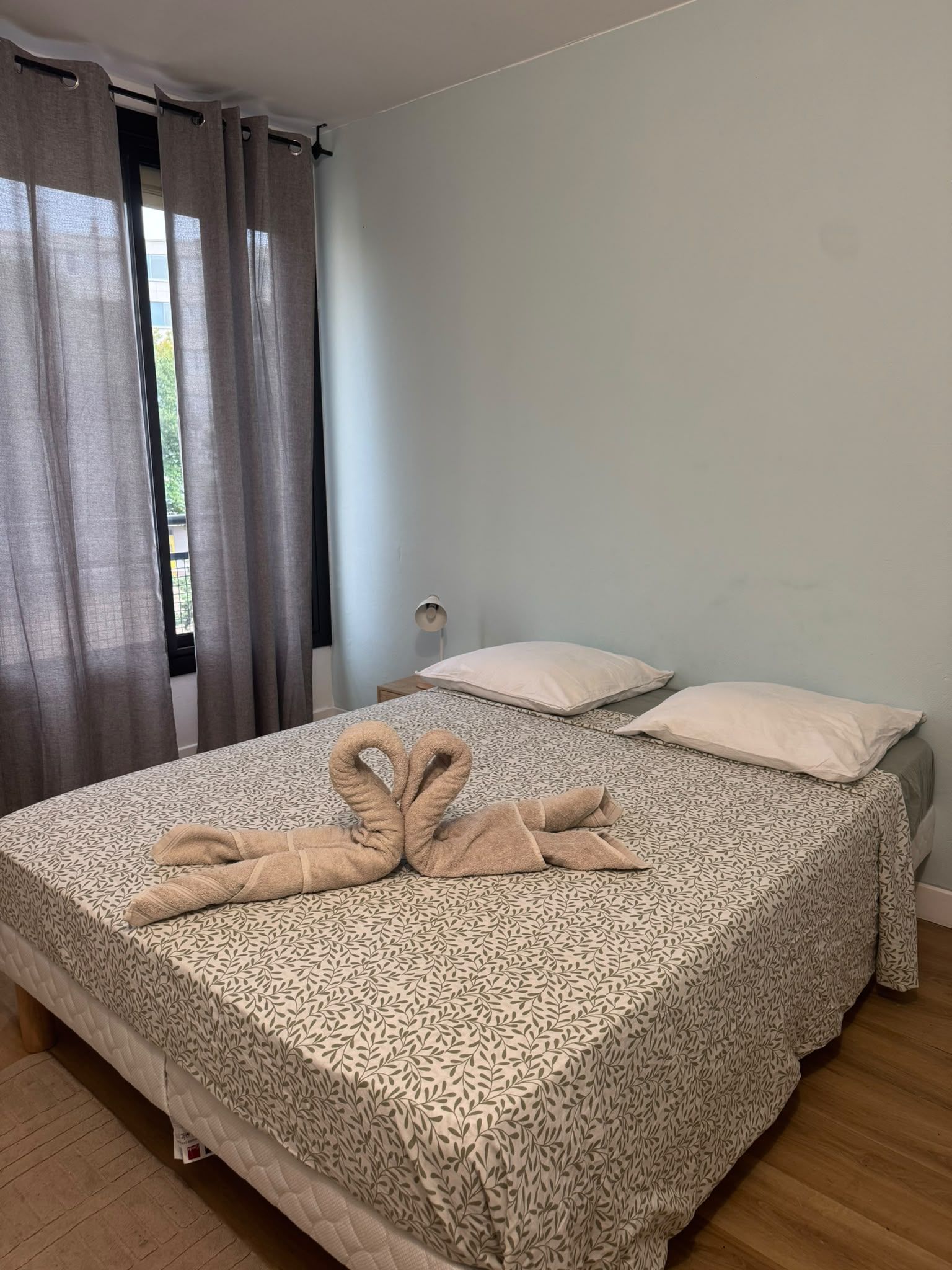 A hotel room with a bed, two pillows, a bedside lamp, and a window with curtains.